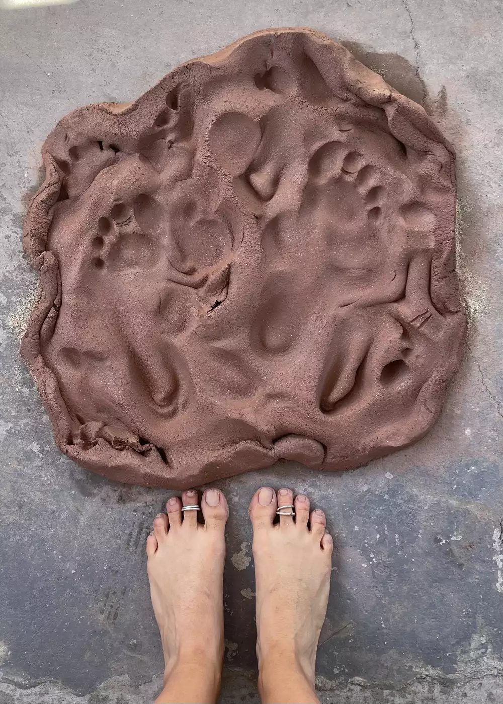 A pair of feet on the floor next to a piece of clay that has been repeatedly stepped on