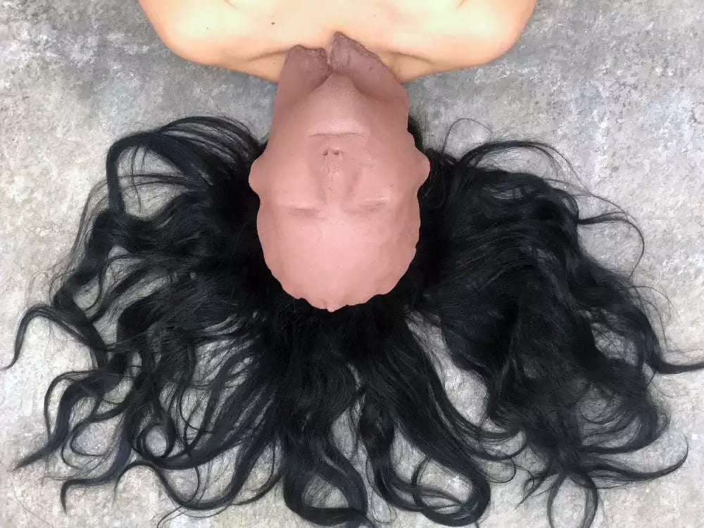 The artist lying on the floor with a piece of clay moulder over her face