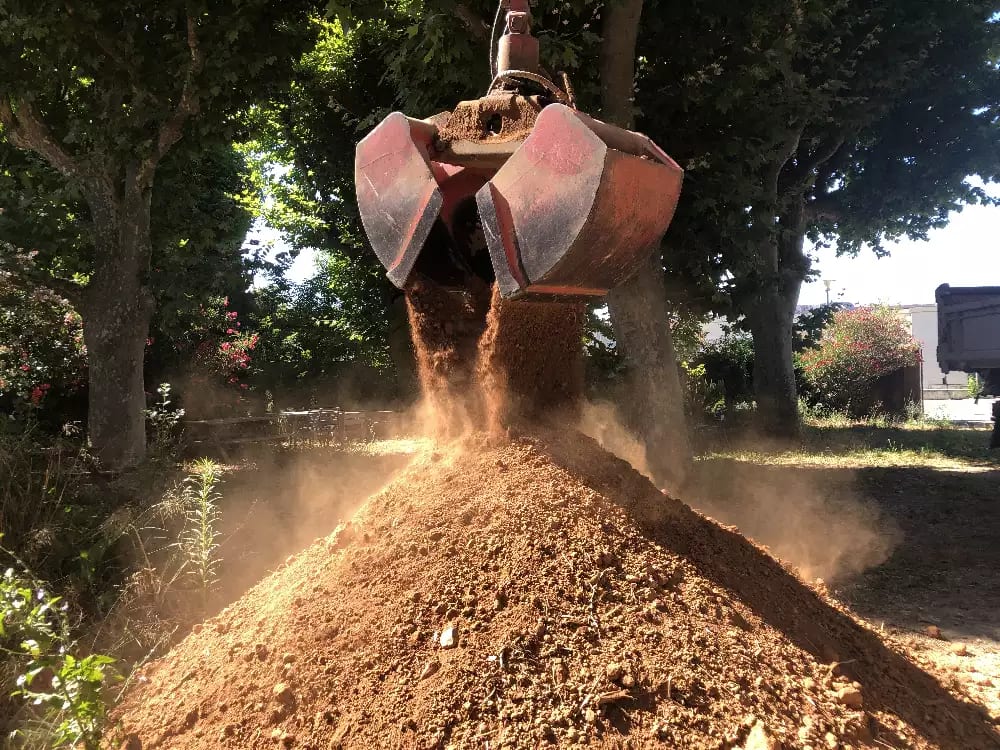 Clamshell grapple scoop unloading soil onto an existing pile outdoors