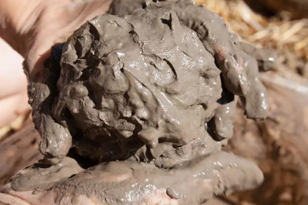 Wet, grey soil being rolled into a ball by hands
