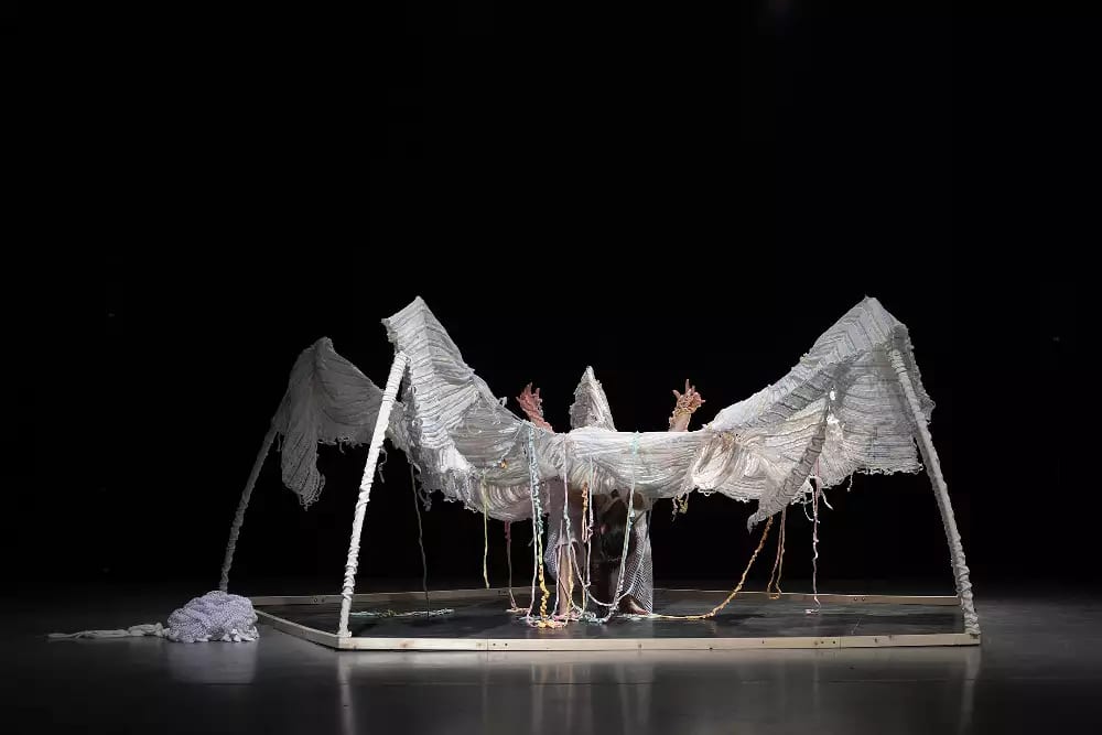 The yarn is propped up by four poles, the woman in bending over in the centre, with her arms in the air